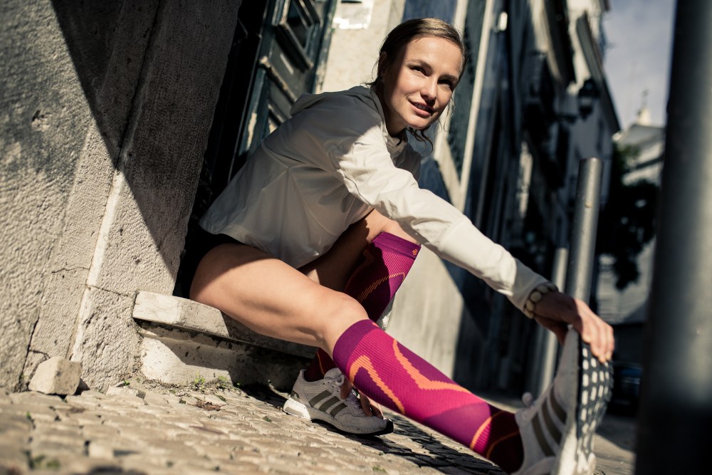 Young woman stretching while wearing Bauerfeind's Run Performance Compression Socks before an inner-city run.