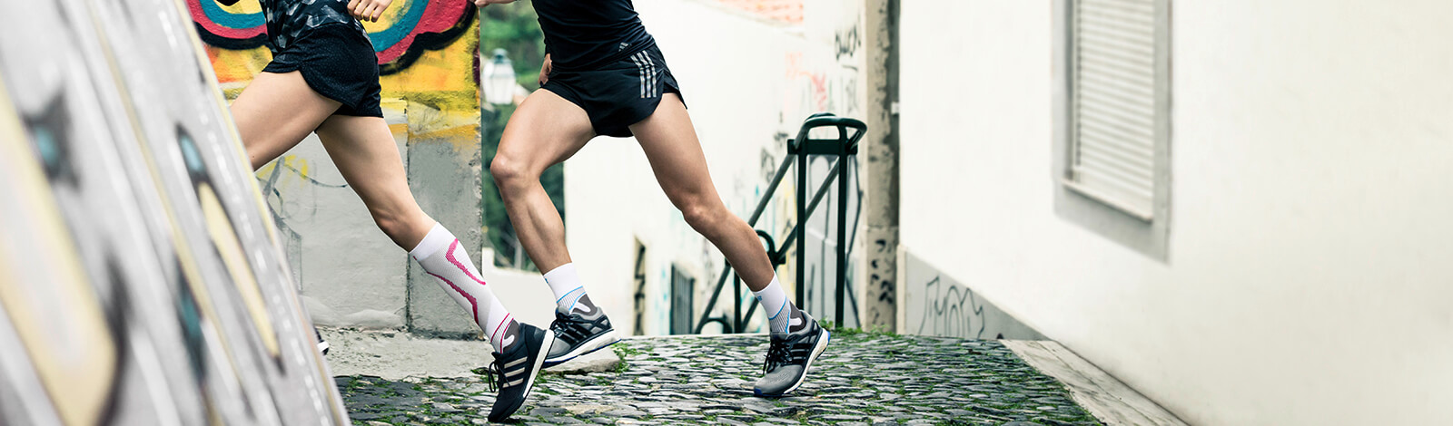 Three young adults wearing Bauerfeind's Run Performance Compression Socks while running uphill in an inner-city street.