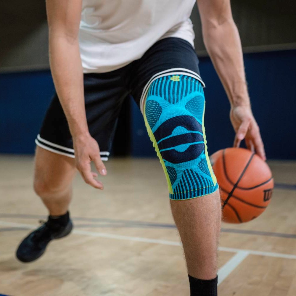 Athlete wearing a knee brace while dribbling a basketball on an indoor basketball ourt