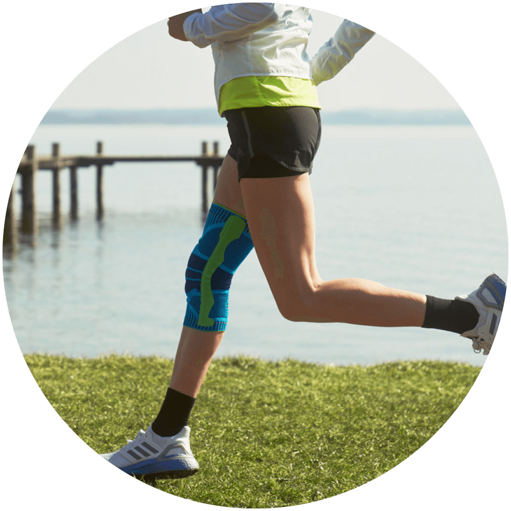 Woman running on grass beside a lake while wearing Bauerfeind's Sports Knee Support.