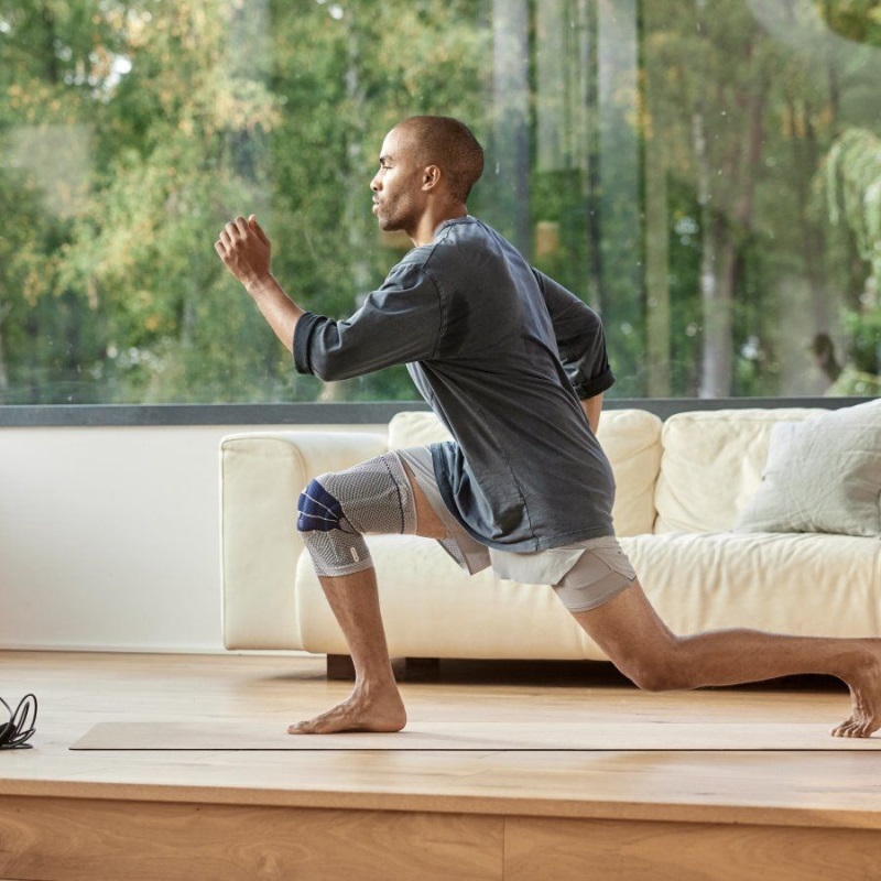 Man performing lunges during an in-home workout while wearing Bauerfeind's GenuTrain knee brace.