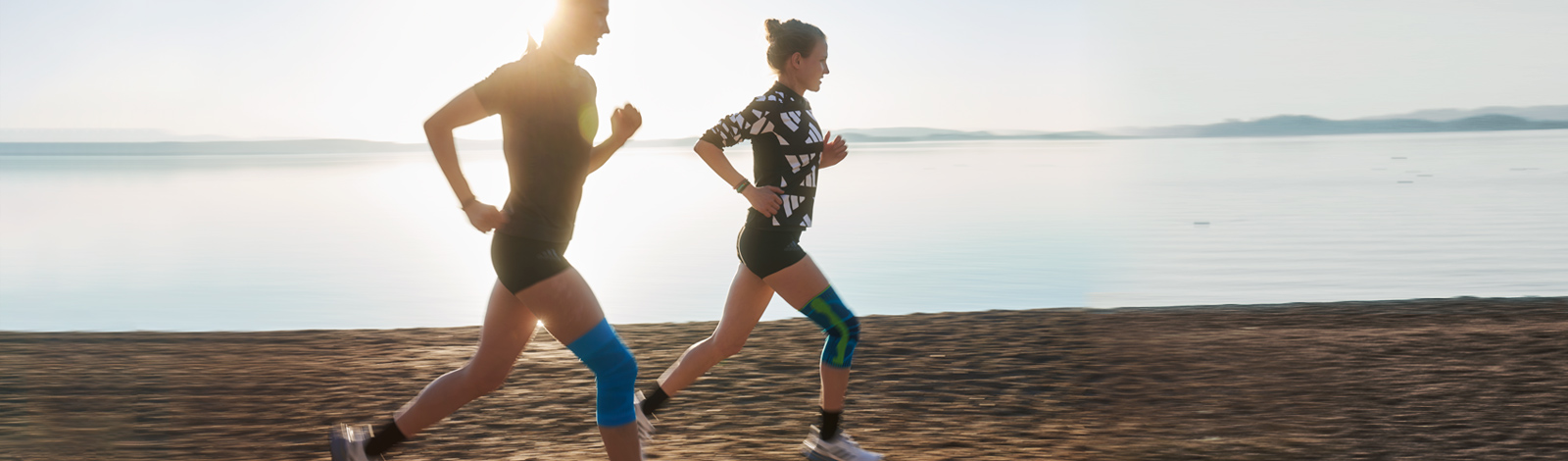 Banner showing two women running near a lake, with the runner on the left wearing Bauerfeind's Sports Compression Knee Support and the runner on the right wearing the Sports Knee Support.