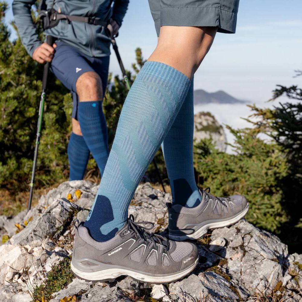 Two hikers on a rocky mountain trail wearing blue compression socks and hiking shoes.