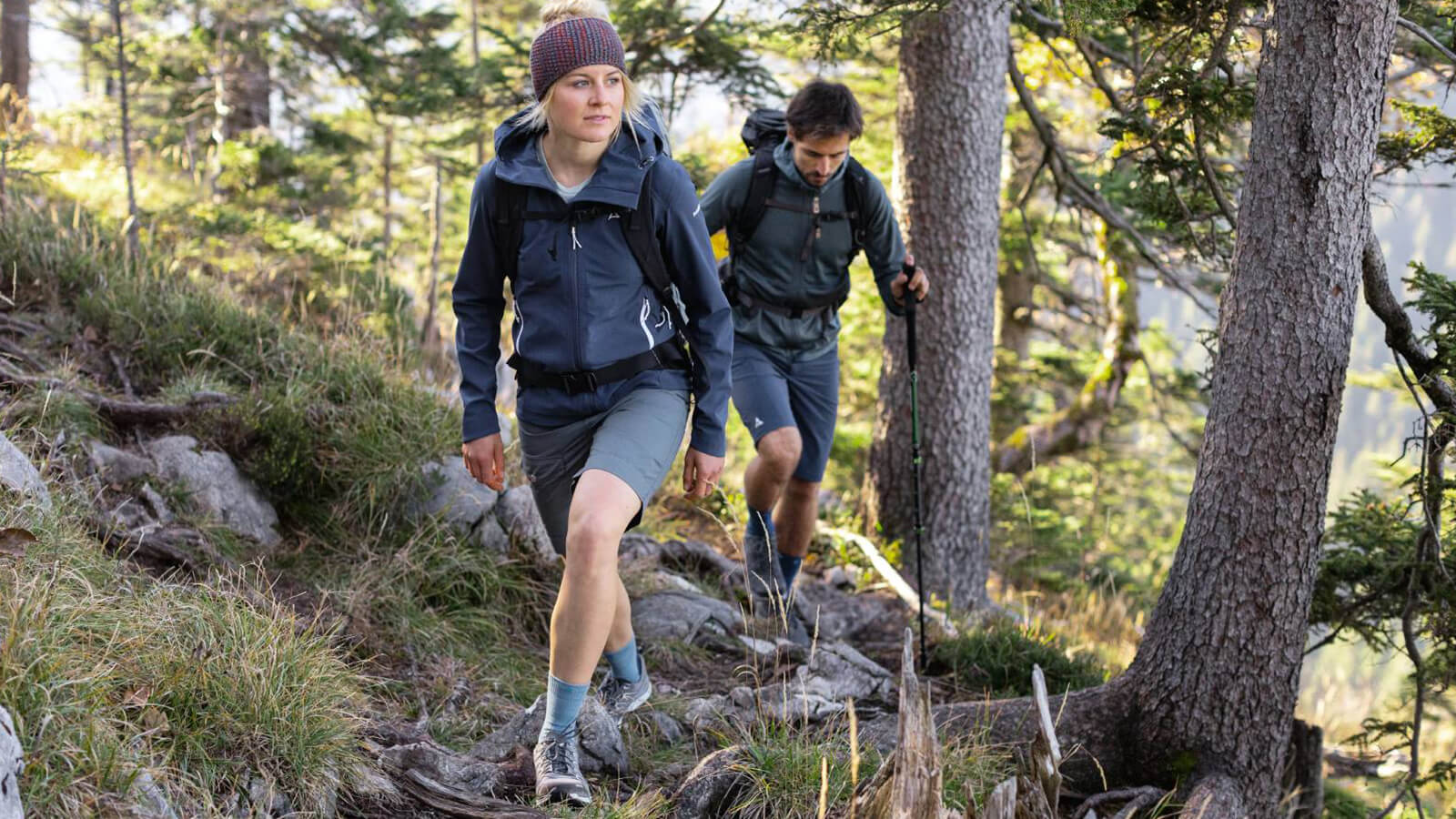 Two hikers wearing a pair of Bauerfeind's Outdoor Merino Mid Cut Socks while trekking through a narrow rocky trail.