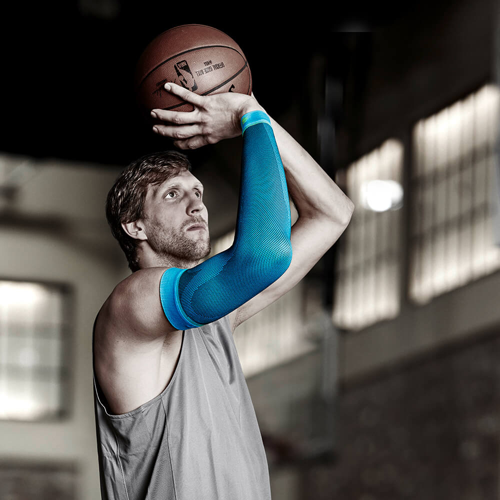 Dirk Nowitzki shooting a basketball while wearing Bauerfeind's Sports Compression Arm Sleeves.