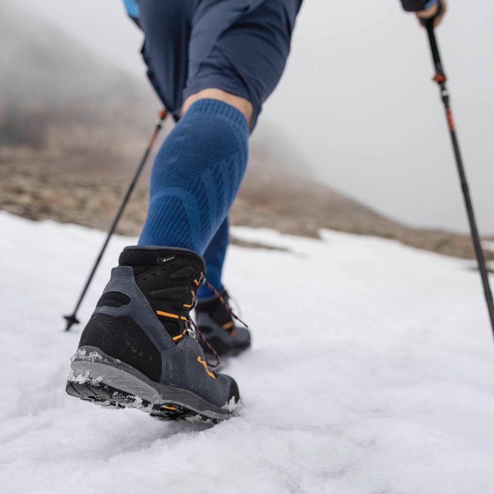 Close-up of a hiker's boots and trekking poles while walking on a snowy mountain trail.