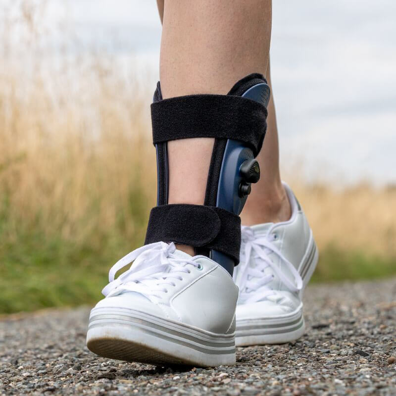 Person walking with white shoes and AIrLoc ankle stirrup brace on their left leg