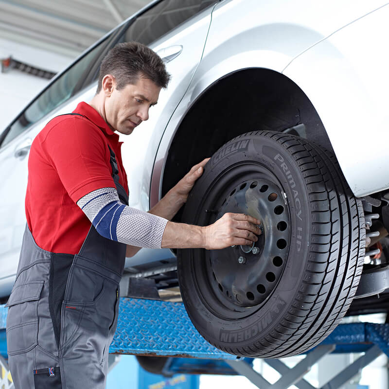 Image of mechanic changing tire while wearing Bauerfeind's EpiTrain elbow brace.