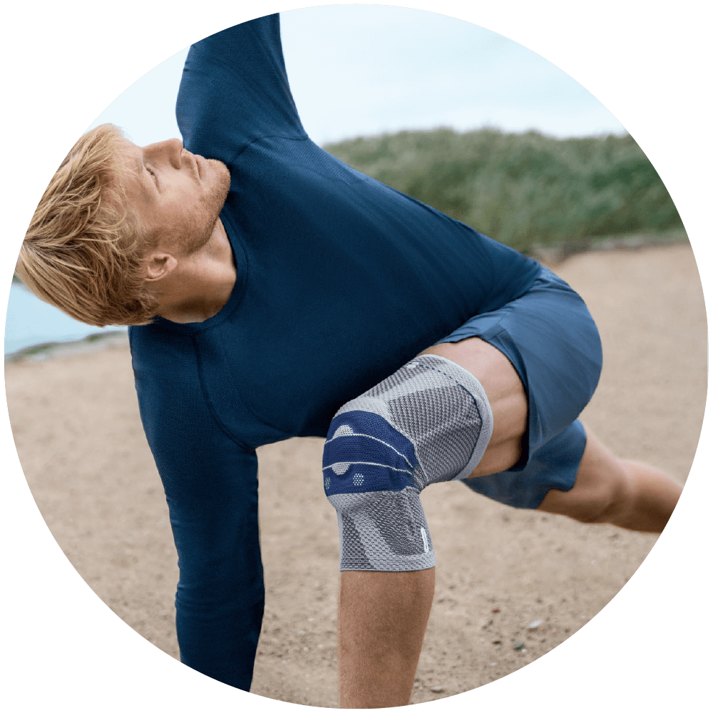 Man practicing yoga while wearing Bauerfeind's GenuTrain knee brace on the beach.