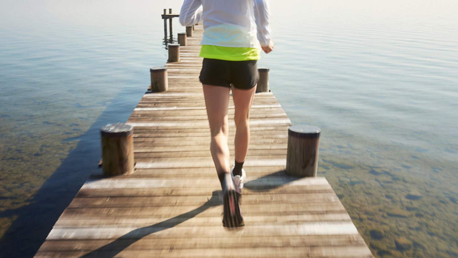 Woman wearing Bauerfeind's Sports Knee Support while running through a forest trail.