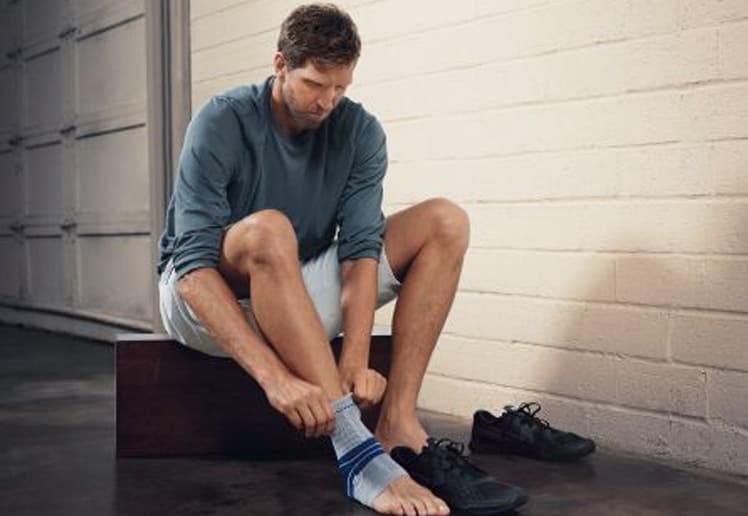 Dirk Nowitzki donning Bauerfeind's MalleoTrain ankle brace before beginning an exercise workout.