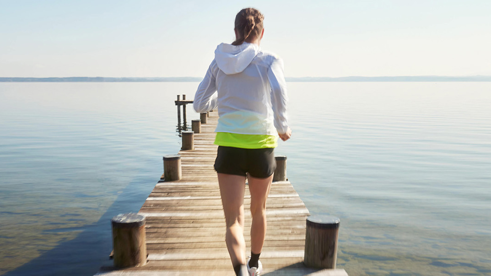 Woman running on a wooden pier over a calm lake.