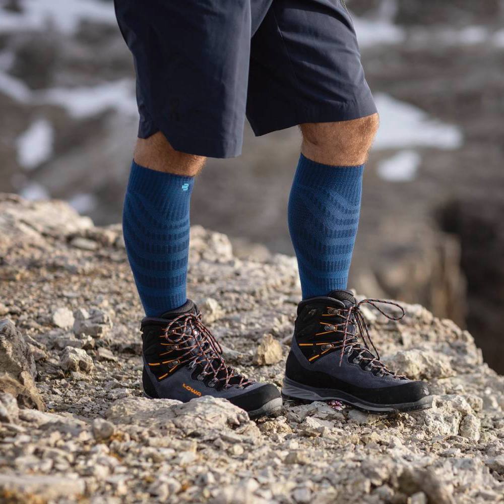 Hiker wearing blue compression socks and black hiking boots standing on rocky terrain