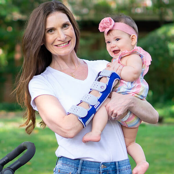 Smiling mother carrying her child during a walk outside while wearing Bauerfeind's ManuLoc long wrist brace.