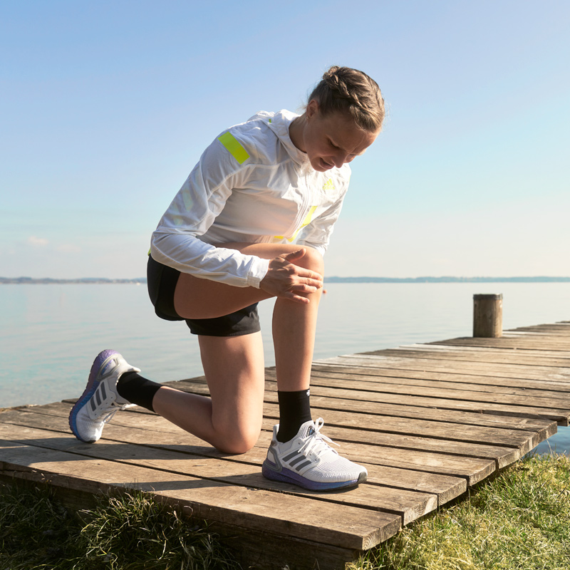 Woman bending down to look at knee while experiencing pain on a morning run.