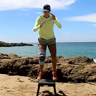 Woman performing box jumps while on the sand near the ocean wearing Bauerfeind's GenuTrain S knee brace.