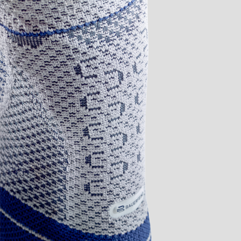 Close-up view of a person wearing a blue and white ankle support brace demonstrating its fit and design on a neutral background