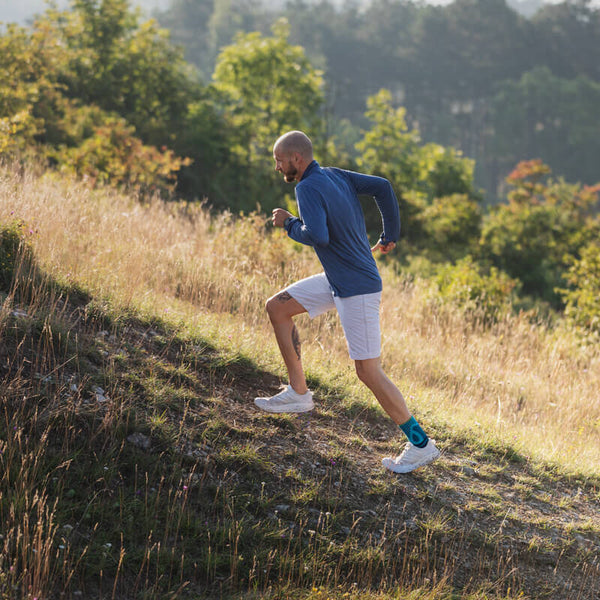 Man donning his shoes while wearing Bauerfeind's Sports Achilles Support before going on a morning jog through a grassy field.