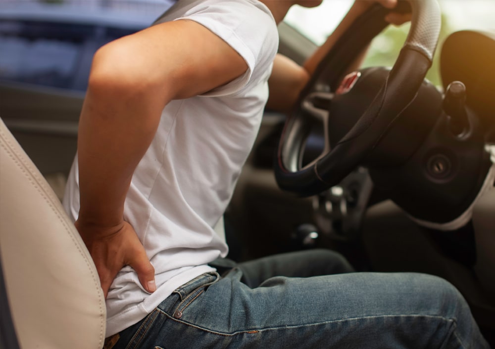 Person experiencing lower back pain while sitting in a car.