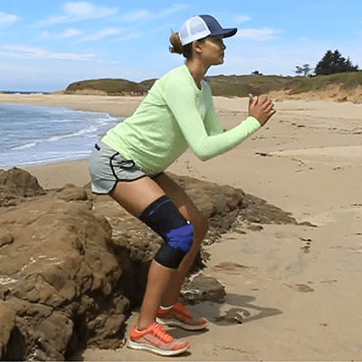 Woman performing the sit-to-stand exercise at the beach while wearing Bauerfeind's GenuTrain knee brace.