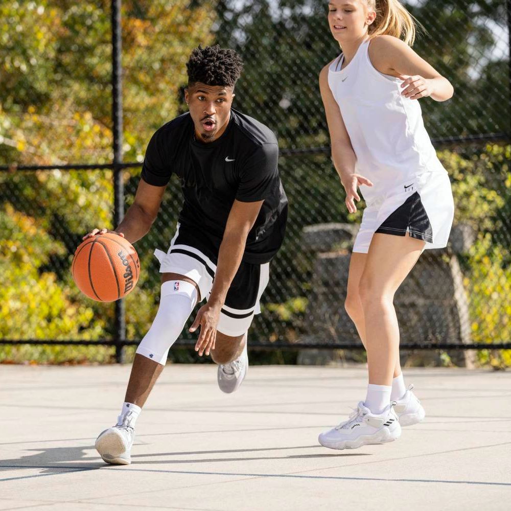 Two athletes playing outdoor basketball on a court, one dribbling the ball while the other defends.