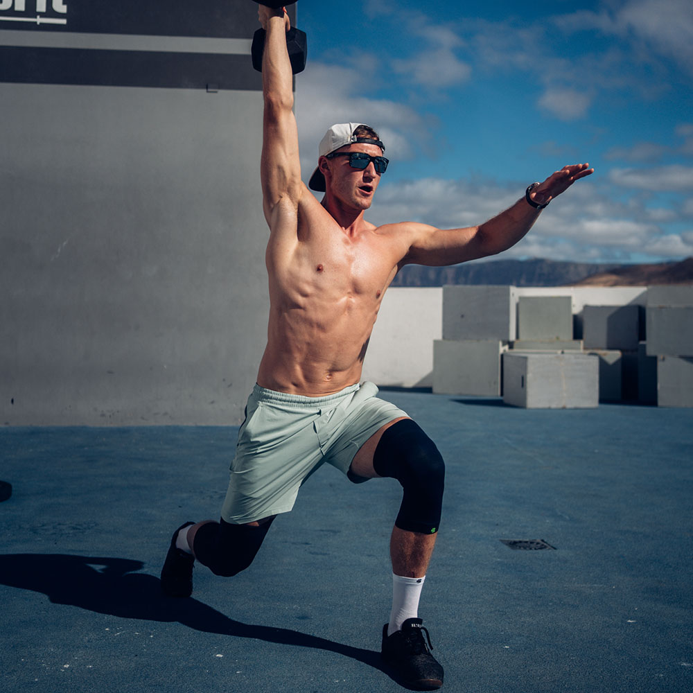 Fit man performing an outdoor exercise holding a dumbbell overhead