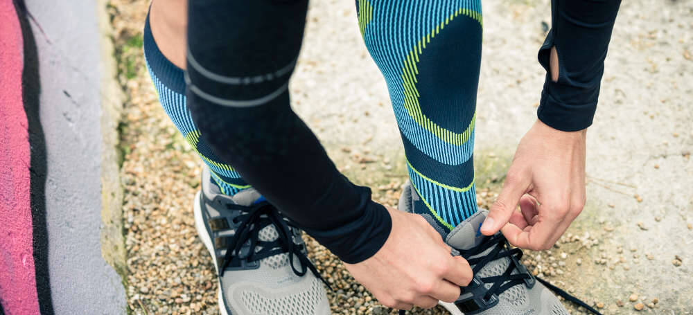 Person tying running shoes before a morning run while wearing Bauerfeind's Run Performance Compression Socks.