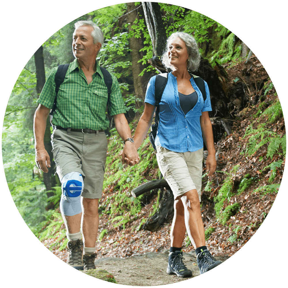 Elderly couple walking through the forest while man wears Bauerfeind's GenuTrain A3 arthritis knee brace.