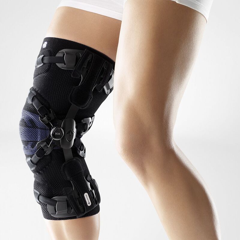 Close-up of a person adjusting a modern black knee brace with straps and orthopedic support on their left knee.