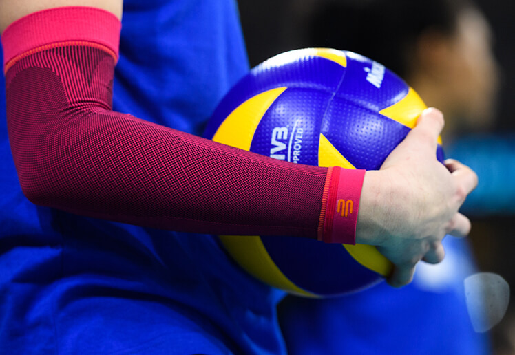 Volleyball player wearing Bauerfeind's GenuTrain P3 patella knee brace while digging the ball toward a teammate.