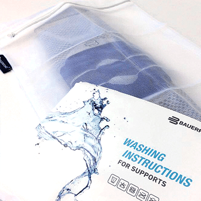 Close-up of a white Bauer athletic support garment with a mesh texture, beside its washing instructions booklet featuring a water splash design.