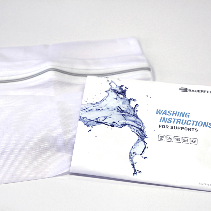 A Bauerfeind washing instructions booklet with a dynamic blue water splash graphic, placed beside a white fabric support on a light grey background.