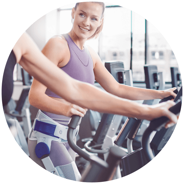 Woman using cardio machine during workout while wearing Bauerfeind's CoxaTrain hip brace.