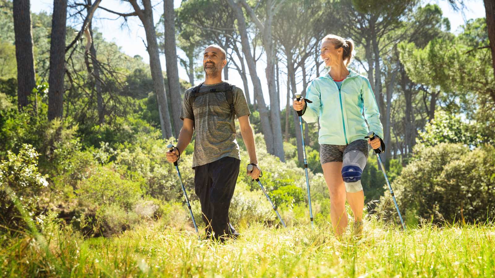 Couple hiking through a grassy trail with the woman wearing Bauerfeind's GenuTrain A3 arthritis knee brace.