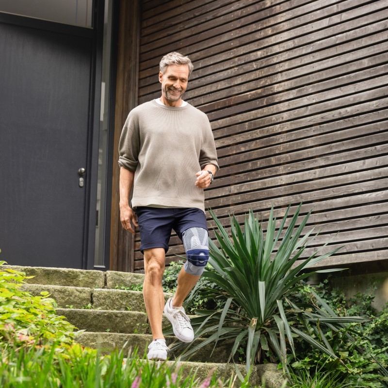 Man leaving his house by walking down steps wearing Bauerfeind's GenuTrain A3 arthritis knee brace.