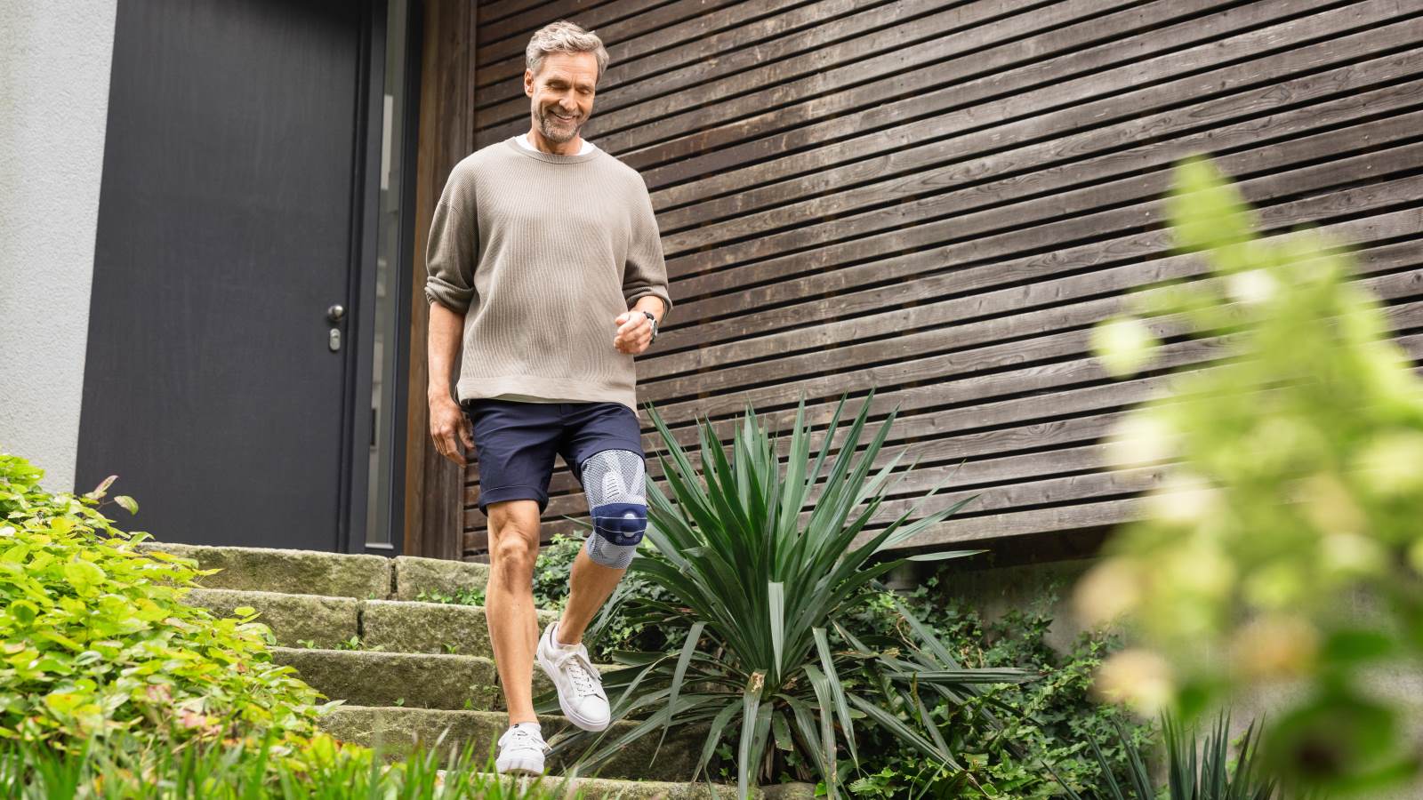 Man leaving his house by walking down steps wearing Bauerfeind's GenuTrain A3 arthritis knee brace.