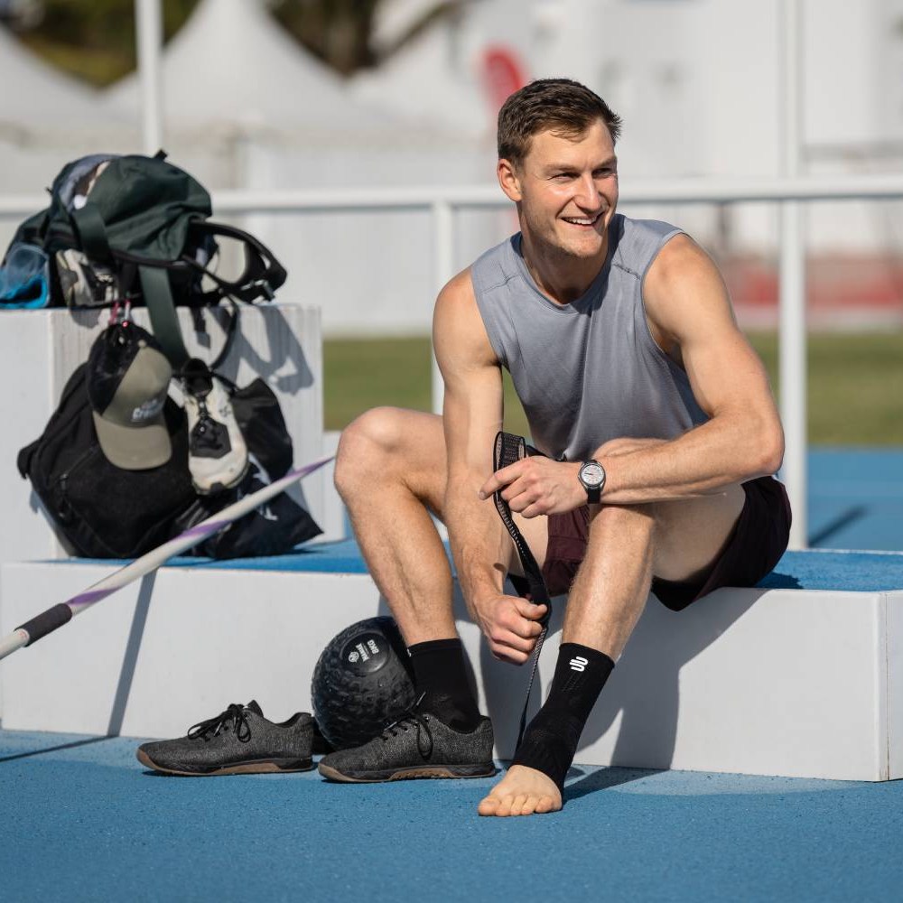 Basketball player wearing black sneakers and colorful socks sitting on an outdoor court with a ball