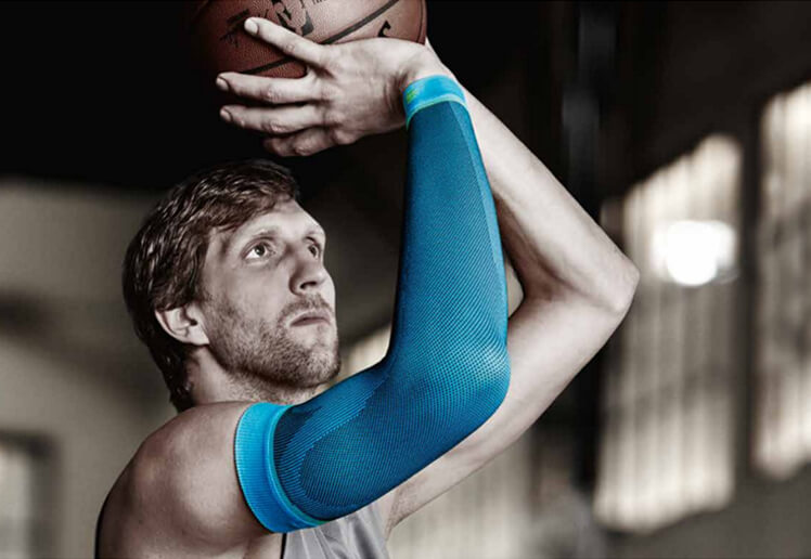 Dirk Nowitzki shooting a basketball while wearing Bauerfeind's Sports Compression Arm Sleeves.