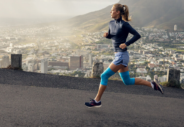 Two women running while one wears Bauerfeind's Sports Knee Support and the other wears Bauerfeind's Sports Knee Strap.