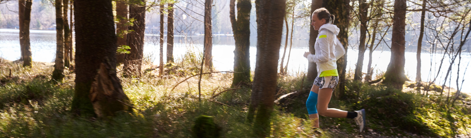 Woman running through a trail while wearing Bauerfeind's Sports Compression Knee Support.