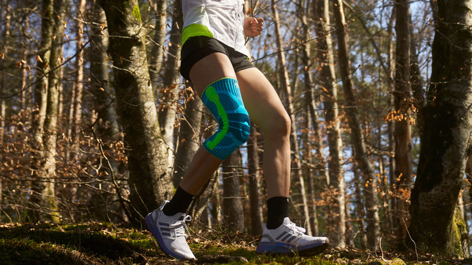 Woman adjusting Bauerfeind's Sports Knee Strap before a morning run through a forest trail.