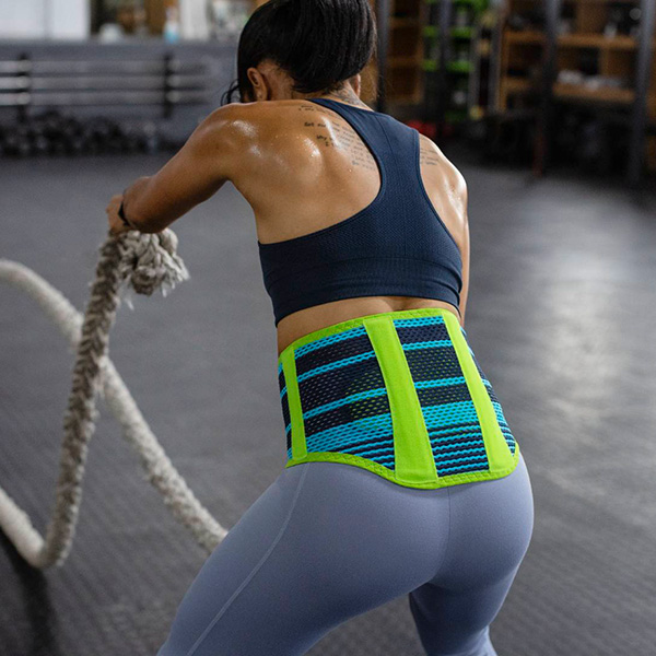 Woman wearing Bauerfeind's Sports Back Support while performing a rope exercise in an indoor gym.