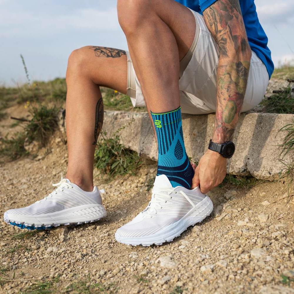 Man wearing the Sports Achilles Support in white sneakers teiing laces