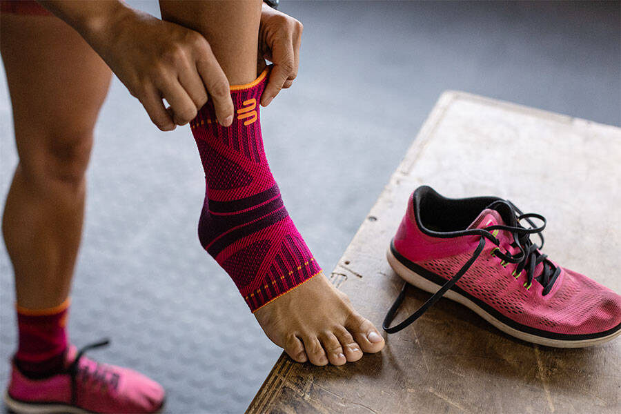 Woman adjusting Bauerfeind's Sports Ankle Support Dynamic before putting on her shoes to exercise.