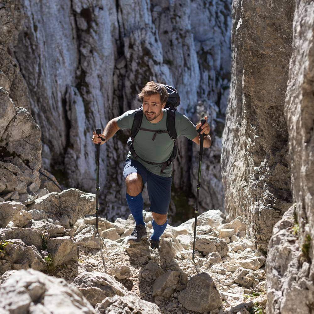 Man hiking in rocky mountain terrain with trekking poles and backpack