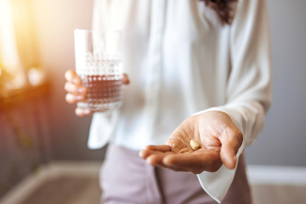 Close-up of a person holding a glass of water and a pill in hand.