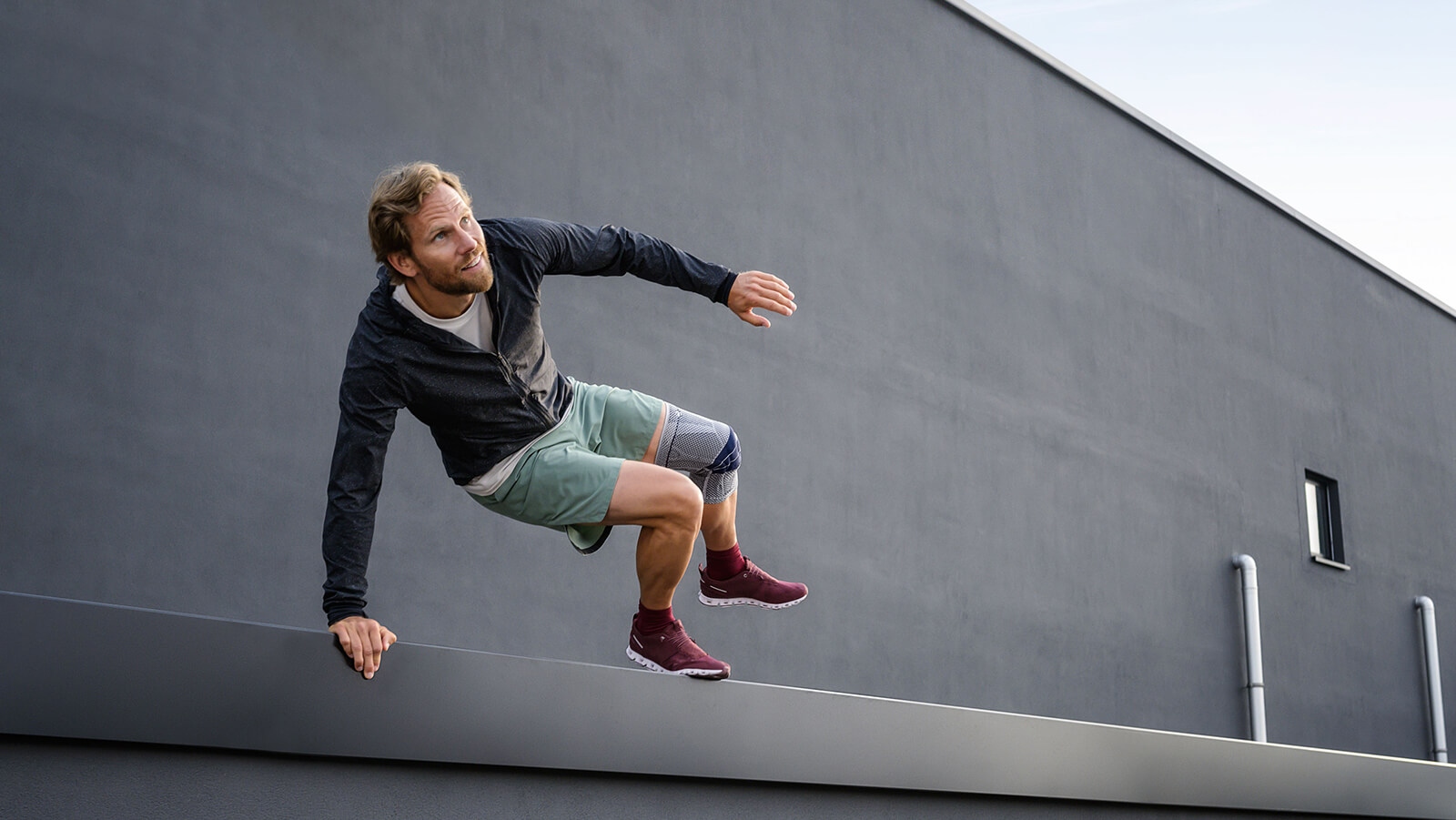 Man jumping over a wall while wearing Bauerfeind's GenuTrain knee brace.