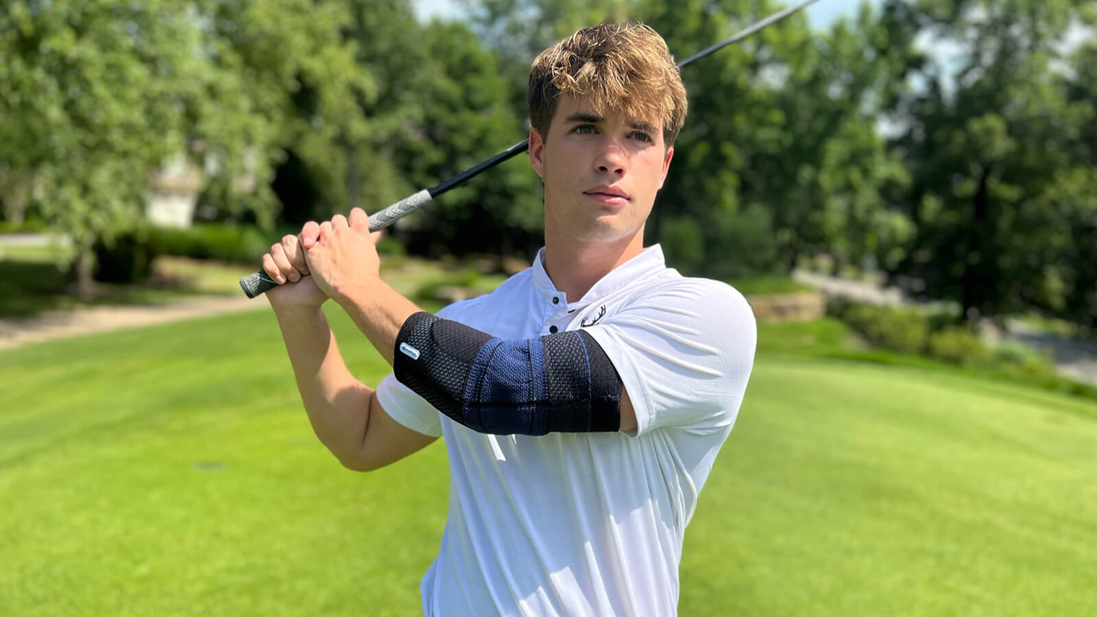 Golfer wearing Bauerfeind's EpiTrain elbow brace while taking a practice swing before teeing off.