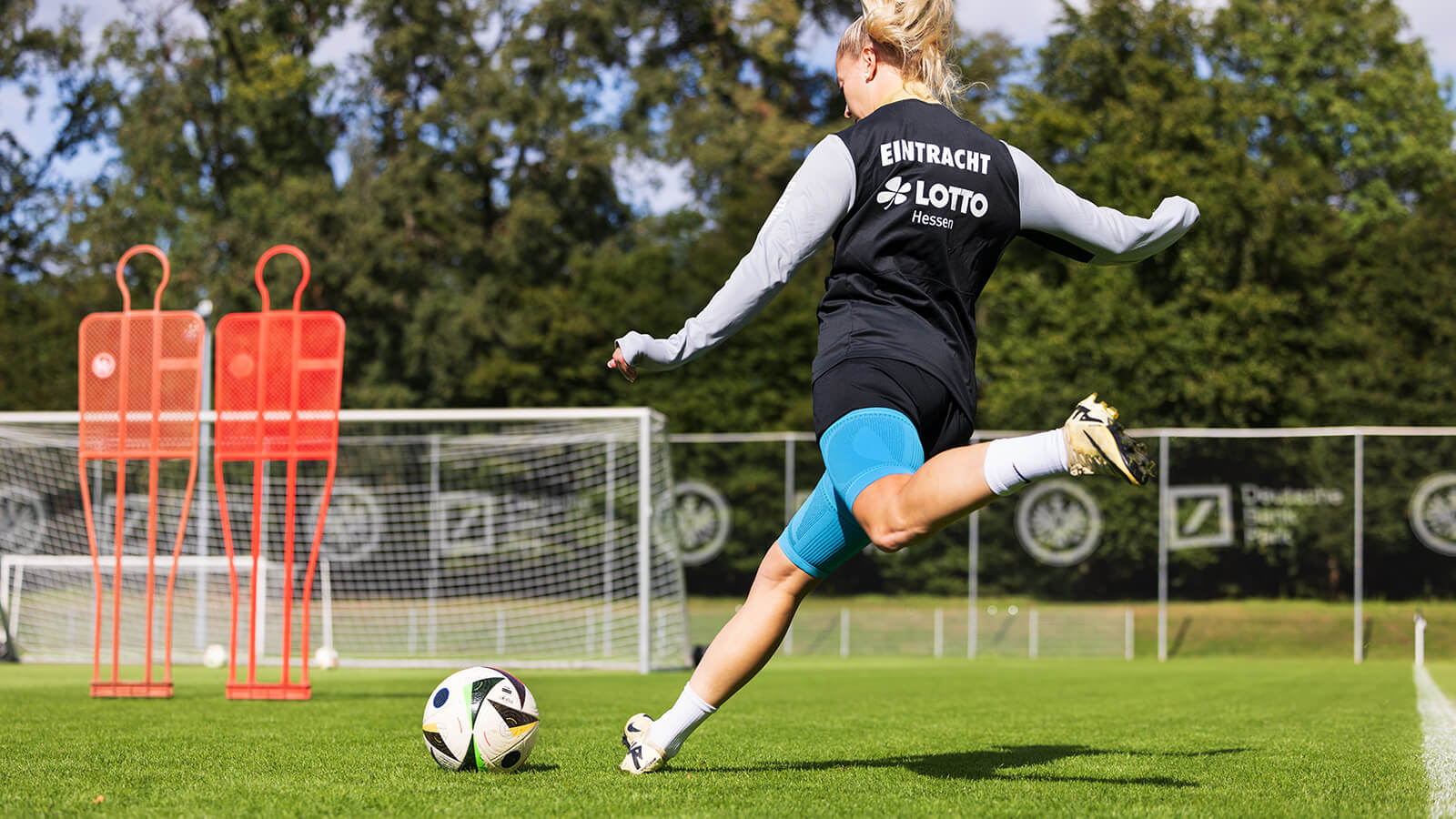 Soccer player wearing Bauerfeind's Sports Compression Upper Leg Sleeves while kicking the ball toward the net.