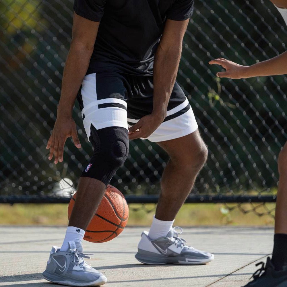 Basketball player dribbling outdoors wearing a knee brace